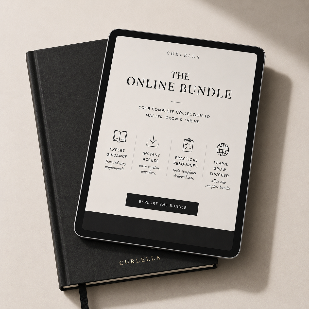 A black Curabella notebook lies open on a light beige surface, with a tablet resting on top. The tablet screen displays a white interface titled 'THE ONLINE BUNDLE' with four feature icons and a black 'EXPLORE THE BUNDLE' button.