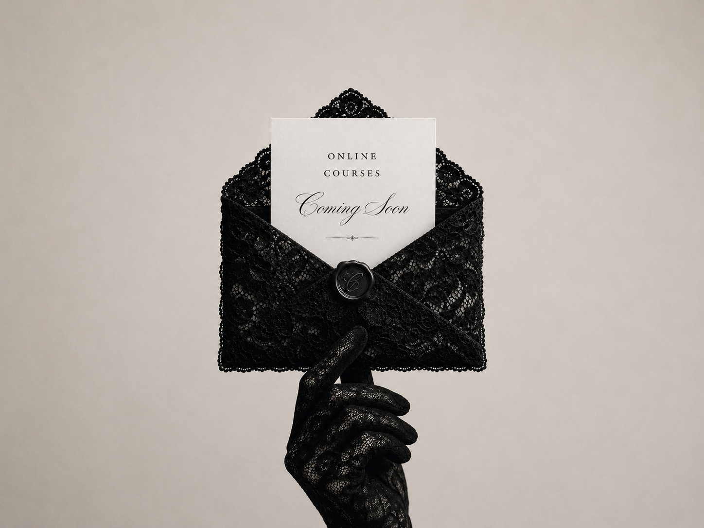 A black lace envelope with a white 'Coming Soon' card tucked inside, held by a hand wearing a matching black lace glove against a plain light beige background.