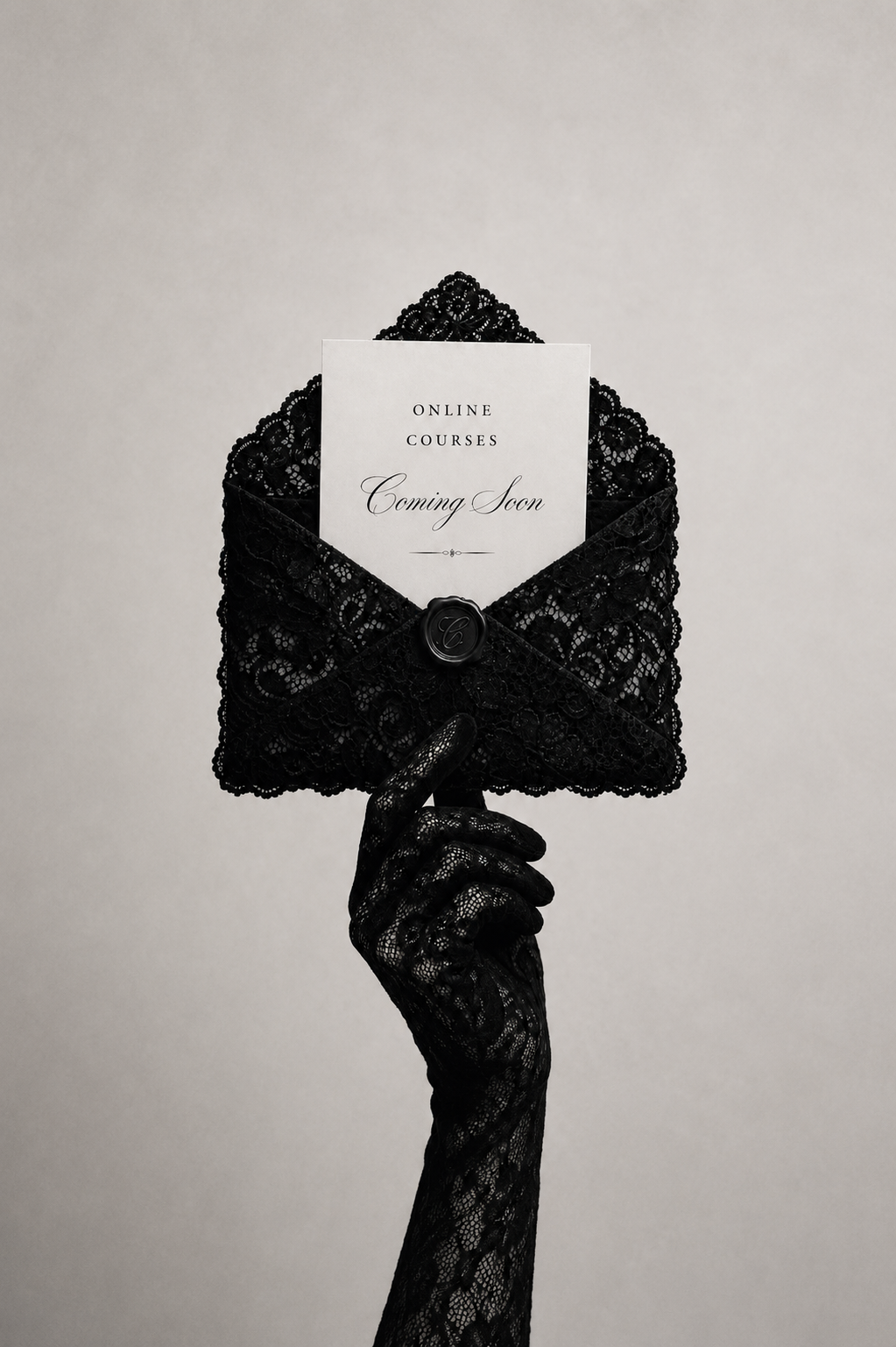A black lace envelope with a lace-covered clasp and a white 'Coming Soon' card, held by a hand wearing a matching black lace glove against a light gray background.