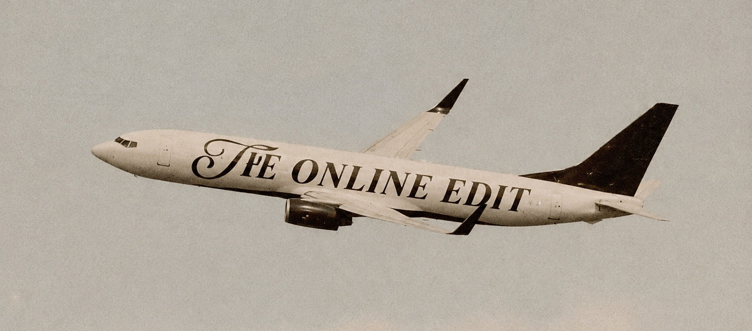A white commercial airplane flying across a pale gray sky, with the words 'The Online Edit' printed in large black script along the side.